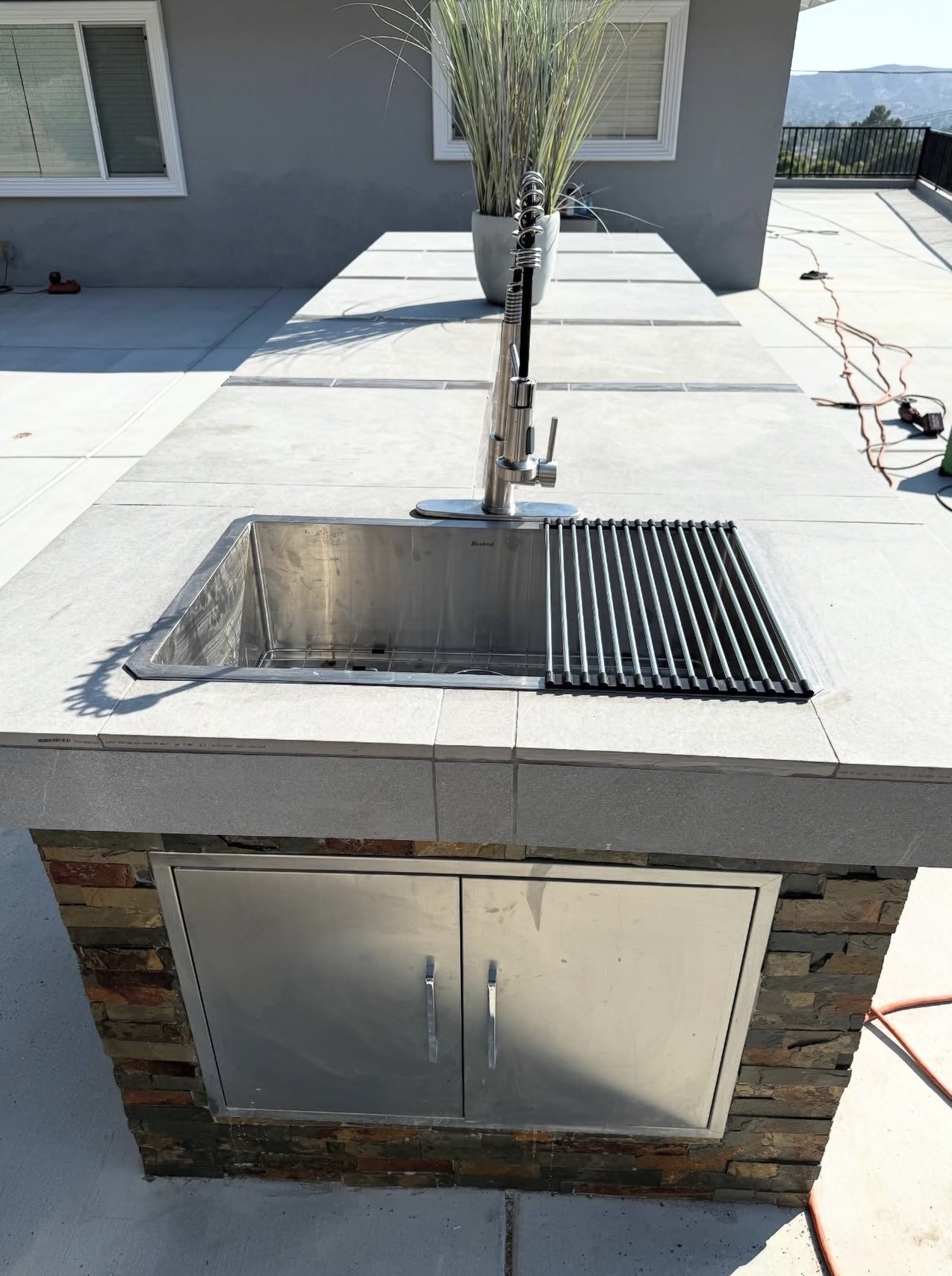 Outdoor kitchen island with stainless undermount sink and pull-down faucet.