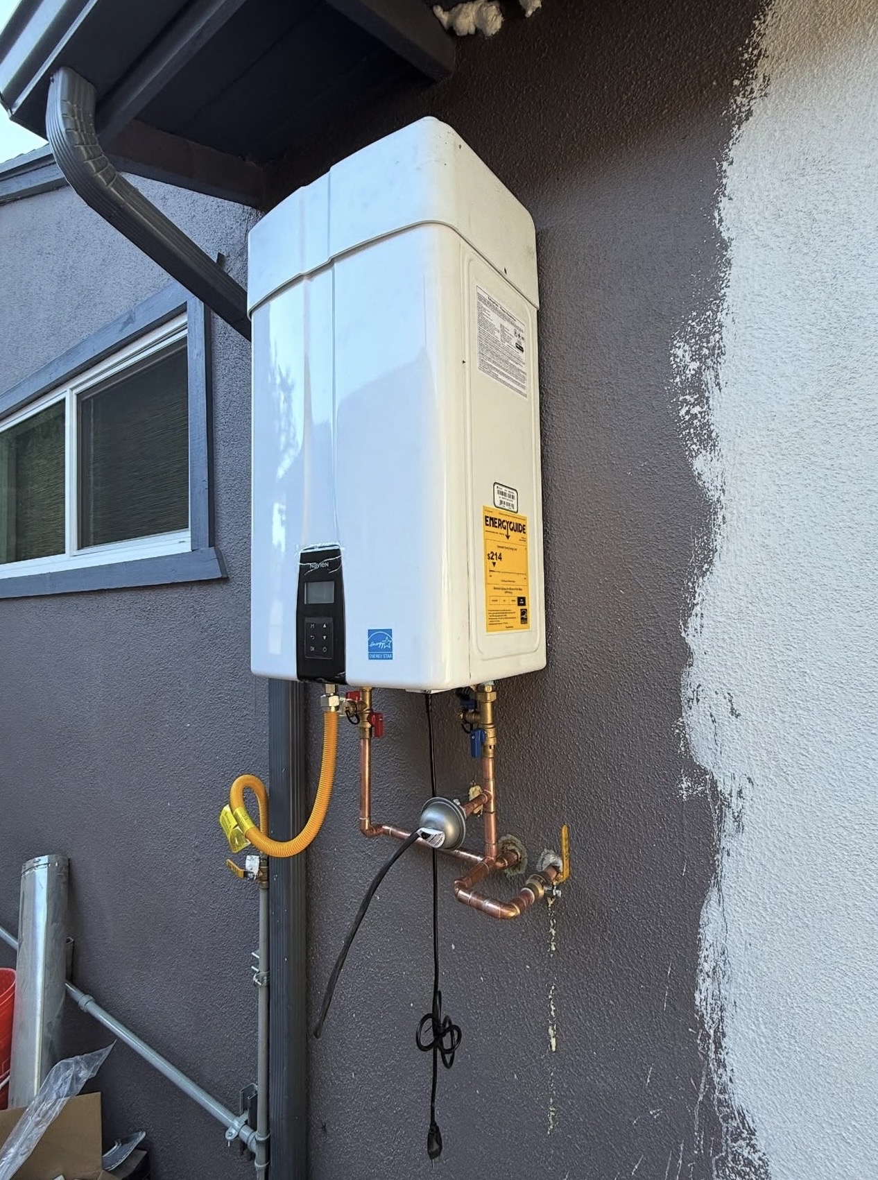 Exterior wall-mounted tankless water heater with copper supply lines and gas connection.